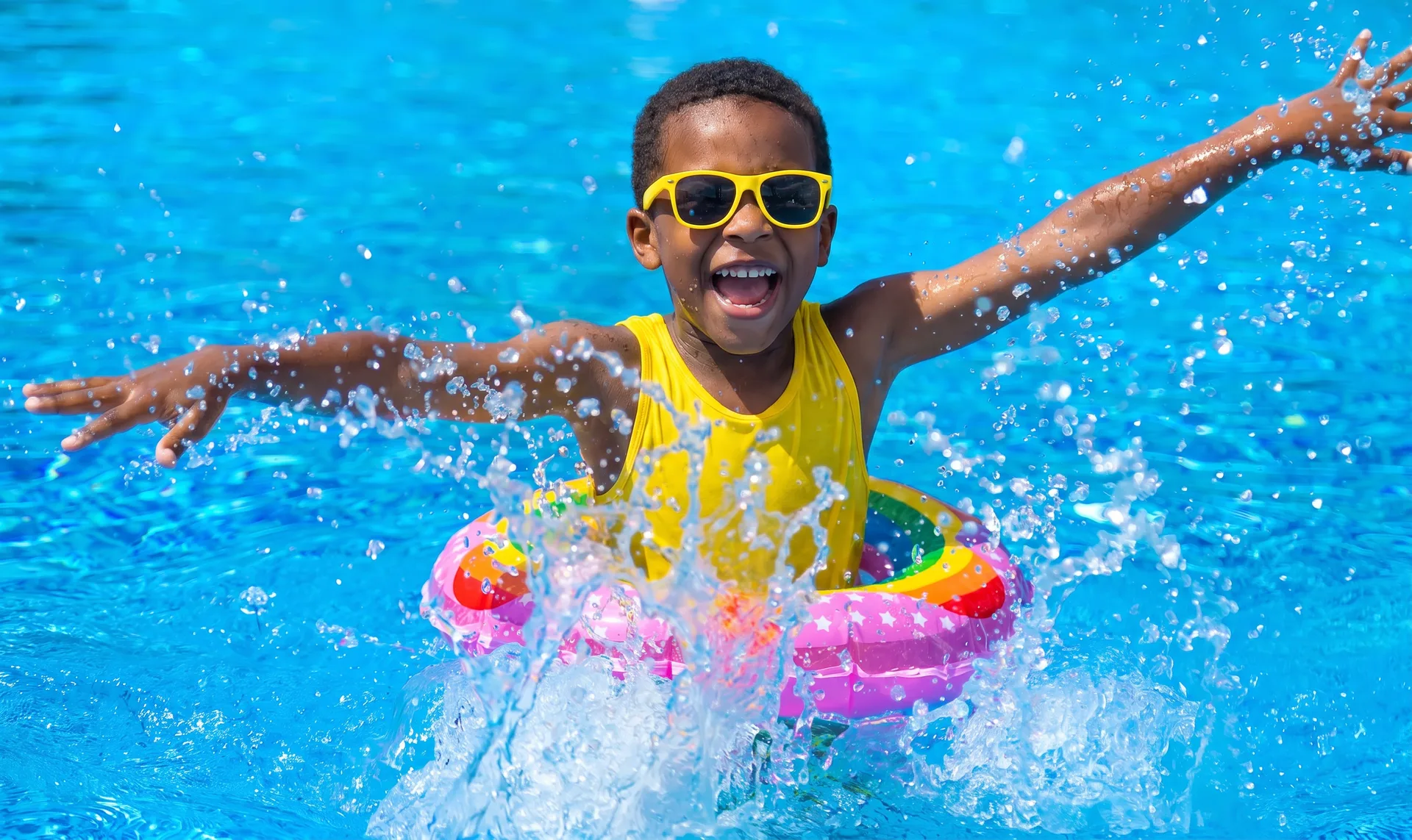 a child with yellow sunglasses splashing in a swimming pool